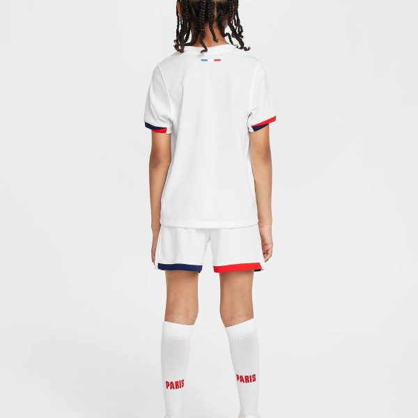Back view of a young athlete in a white soccer jersey and shorts with red/blue trim, red 'PARIS' text on white socks, standing against a light background.