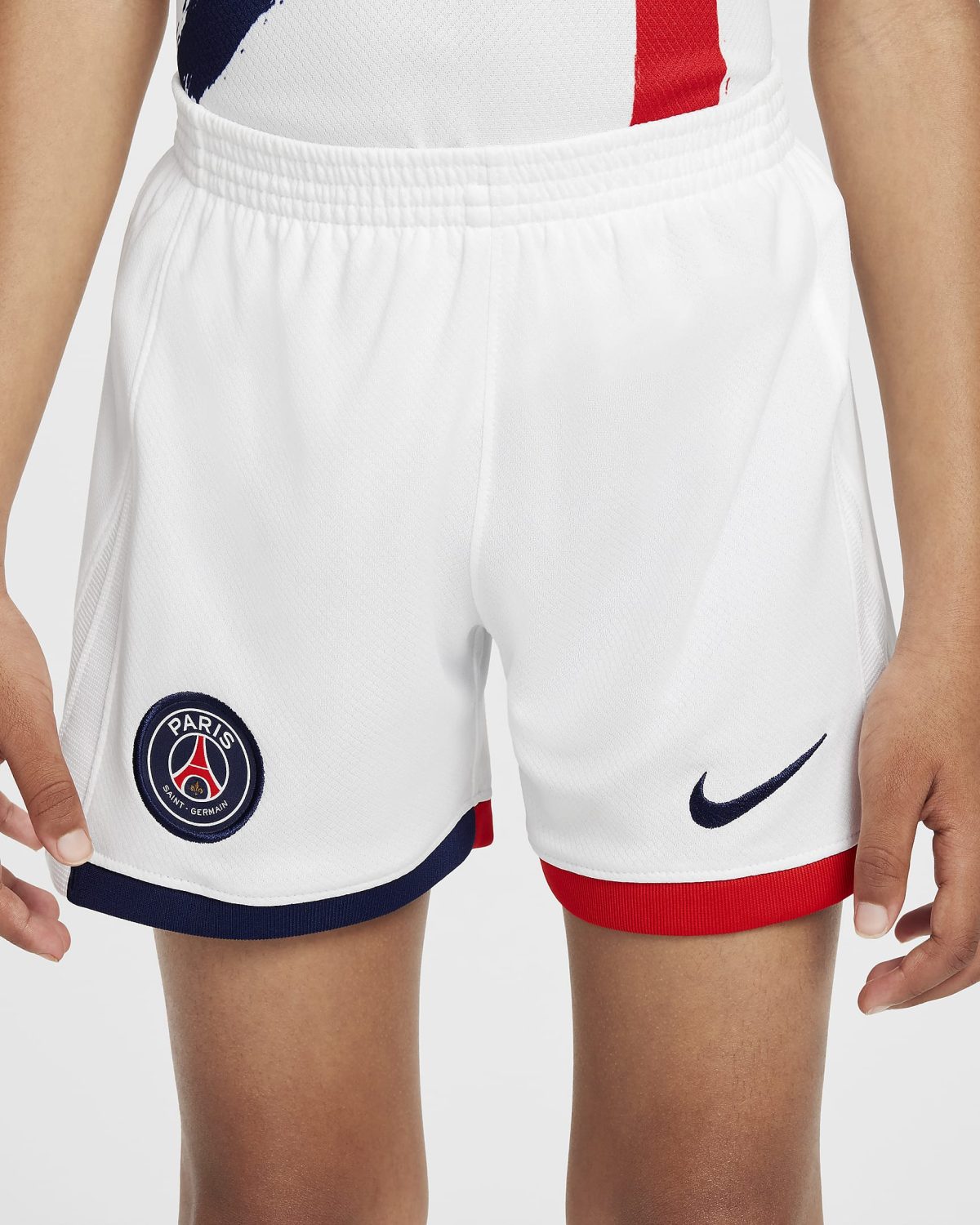 White athletic shorts featuring PSG crest on the left leg with navy trim, worn by a person.