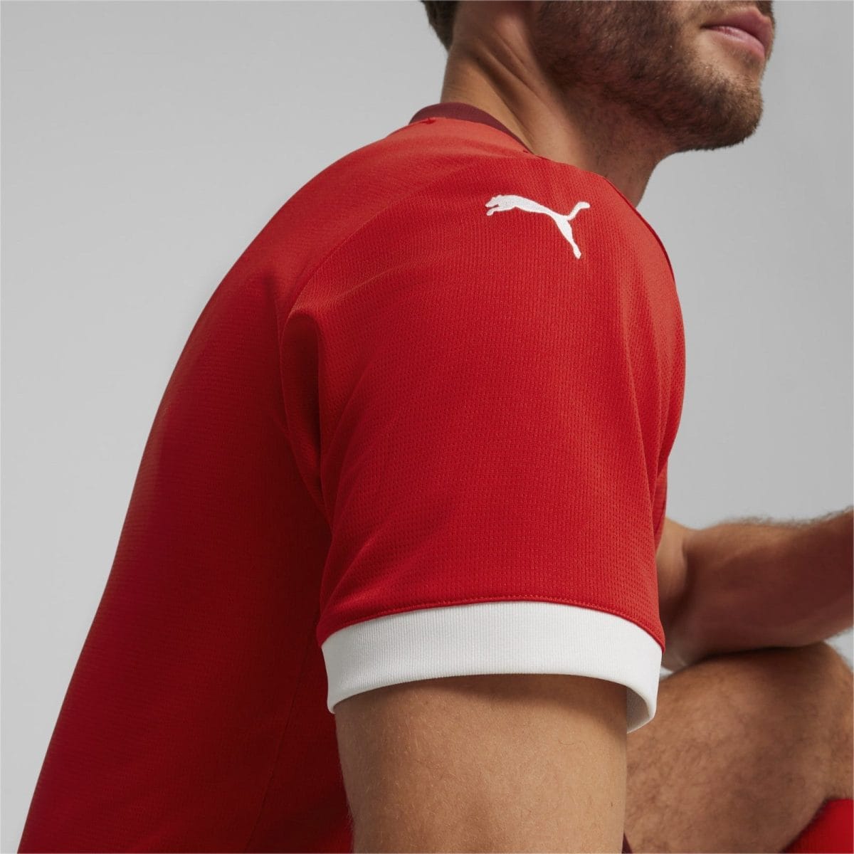 Close-up of a man's red athletic shirt showing the shoulder seam and white cuff against a gray studio background.