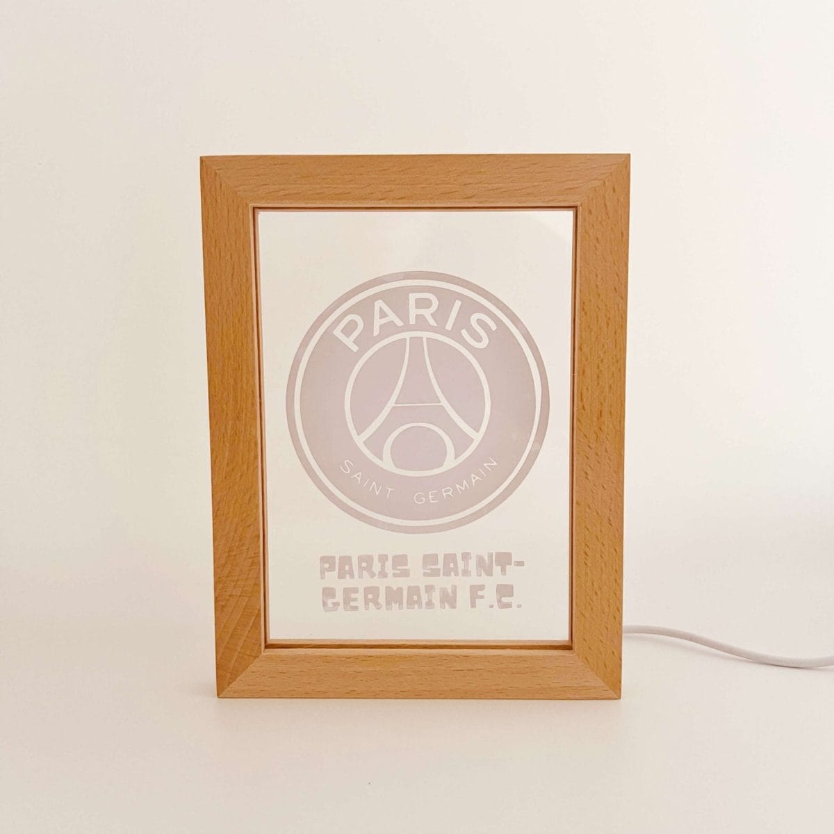 Wooden frame displaying a PSG logo and text Paris Saint‑Germain football club on a white surface.