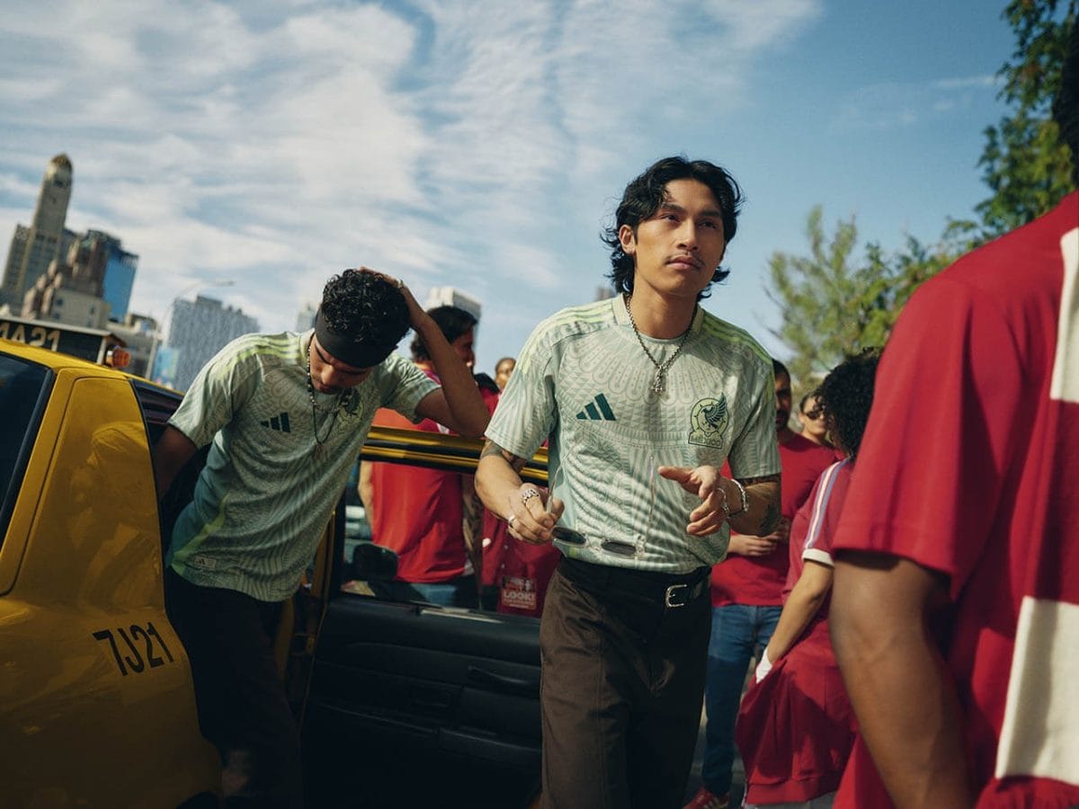 Young man in a light-green jersey stands by an open yellow taxi with a crowd behind him.