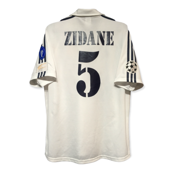 Back view of a white sports jersey with bold letters reading 'ZIDANE' and a large number 5 on the back, with patches on the sleeves.
