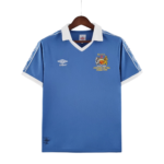 Blue football jersey on a wooden hanger with a white collar, featuring the Umbro logo on the left chest and a crest with Wembley 1981 text on the right.
