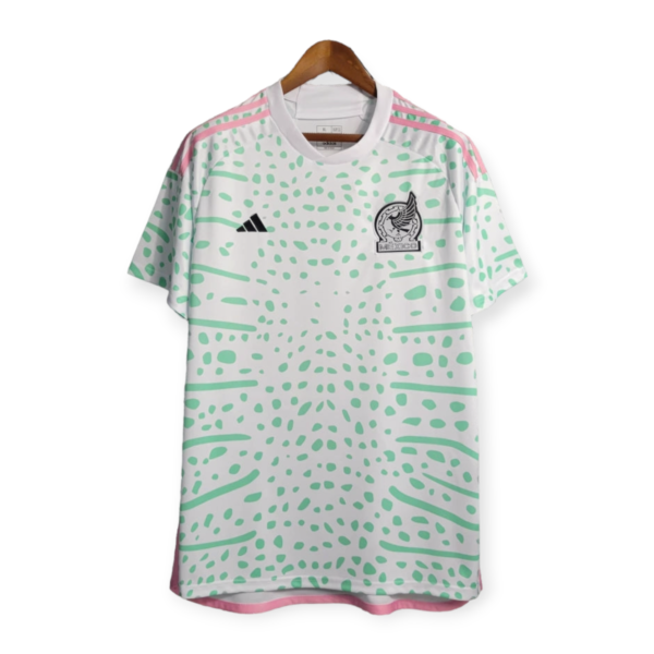 White Adidas jersey with green dot pattern, pink shoulder stripes, and Mexico crest on the chest, hanging on a wooden hanger.