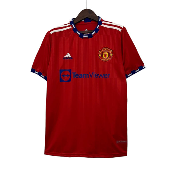 Red Manchester United football jersey on a hanger, showing the club crest, Adidas logo, and TeamViewer sponsor text on the chest area.