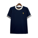 Navy blue dress on a hanger with a white rounded collar and striped white cuffs at the sleeves, front view with crest badge on the chest area.
