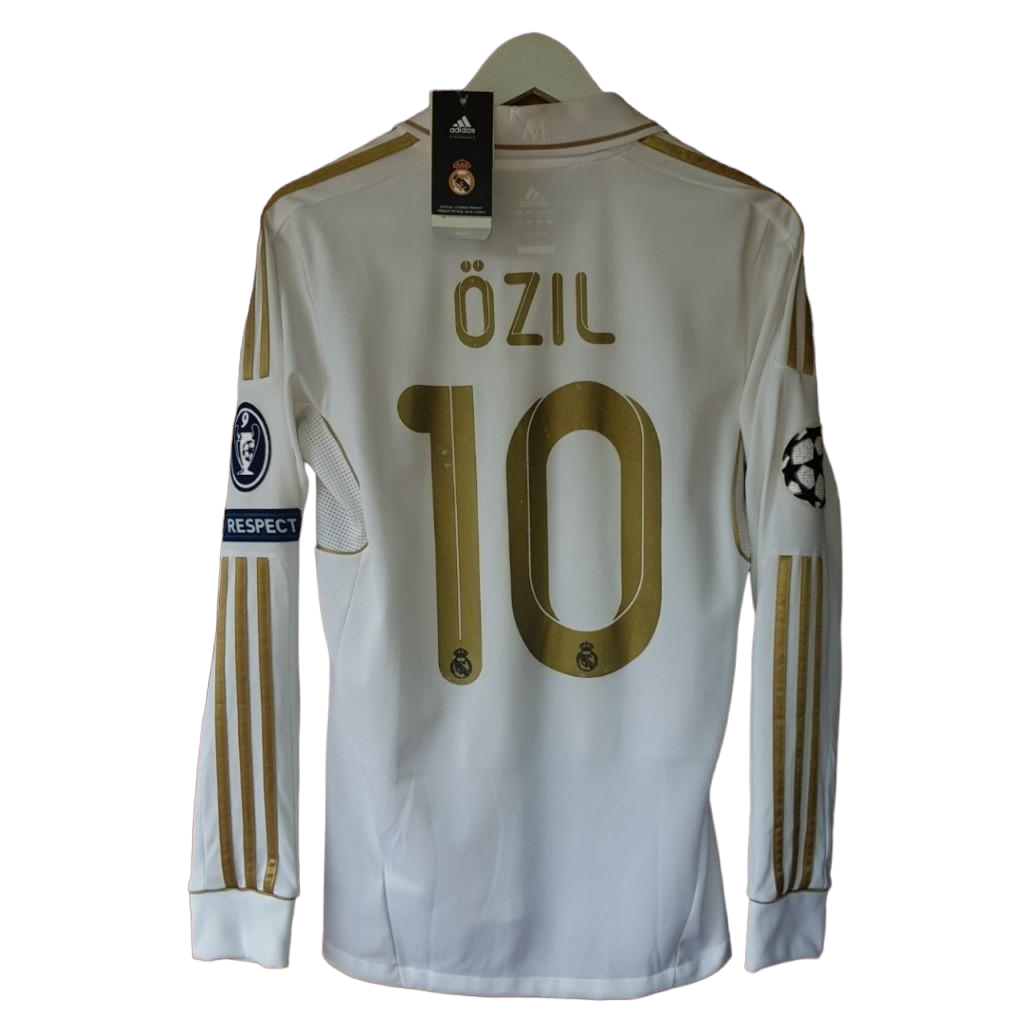 PhotoRoom-20230623_075837_3b70f6da-cb88-4dad-b999-4aa60a87971a White Real Madrid football jersey with gold 'Özil' and number 10 on back, Champions League sleeve patch visible.