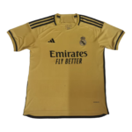 Gold Real Madrid soccer jersey with Emirates Fly Better sponsor, Adidas logo, and club crest on the chest, featuring black shoulder stripes.