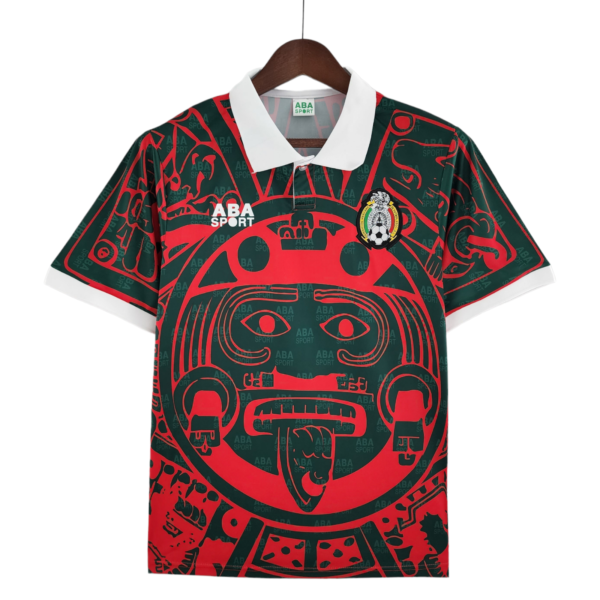 Dark green sports polo with a bold red Aztec-style graphic, white collar, ABA SPORT logo on the left chest, and a Mexican crest badge on the right chest.