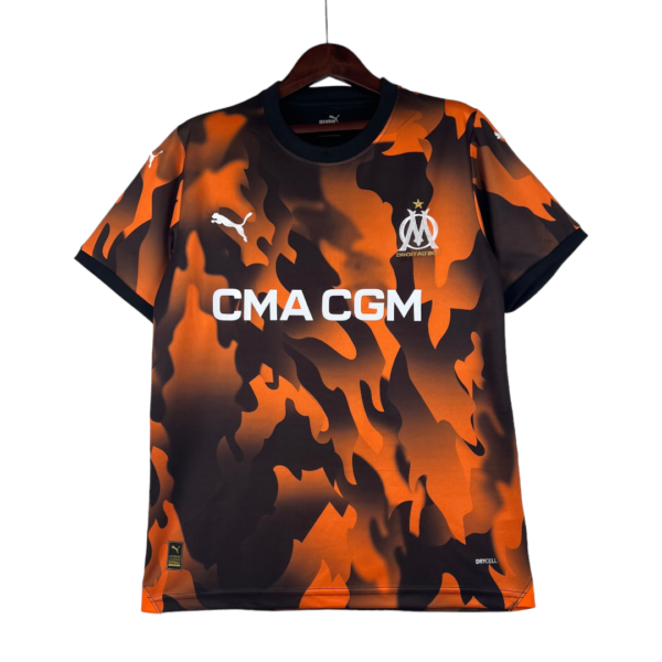 Orange and black camouflage soccer jersey with OM crest and CMA CGM text hanging on a wooden hanger.