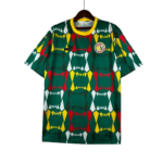 Green geometric-pattern soccer jersey on a hanger with red, yellow, and white diamond shapes, yellow collar, and a circular crest on the chest along with a small brand logo on the opposite side.