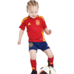 Young child in a red Spain soccer jersey and blue shorts controlling a soccer ball, ready to play.