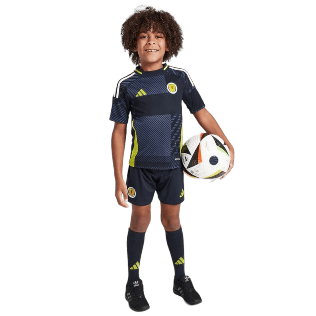 Smiling boy in a dark navy Scotland soccer jersey and shorts, holding a soccer ball at his side.