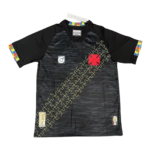 Black athletic jersey with a diagonal yellow puzzle-piece pattern across the front, red square emblem near the chest, and multicolor puzzle-piece cuffs on the sleeves.