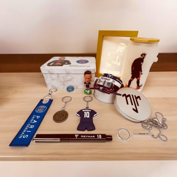 Neymar Jr. memorabilia on a wooden table: keychains, a blue PSG lanyard, a small figurine, and a framed print alongside other souvenirs.