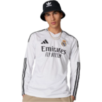 Young man wearing a white Real Madrid long-sleeve jersey with Emirates Fly Better logo and black Adidas stripes, paired with a black bucket hat and beige pants.