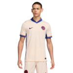 Young man wearing a Chelsea FC cream soccer jersey with blue collar, standing against a white background, crest visible on chest.
