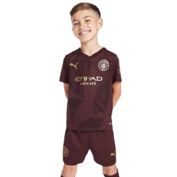 Smiling boy in a maroon soccer jersey with gold logos, standing with hands behind his back