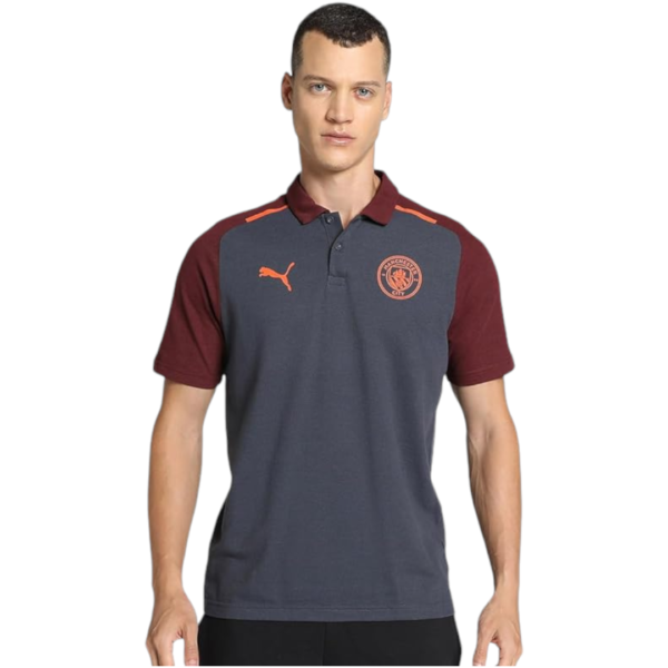 Male model wearing a navy polo shirt with maroon sleeves and collar, featuring an orange Puma logo and Manchester City crest on the chest.