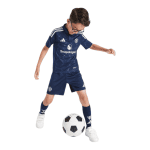 Young boy in a dark blue soccer uniform controlling a soccer ball mid-dribble on a white background.