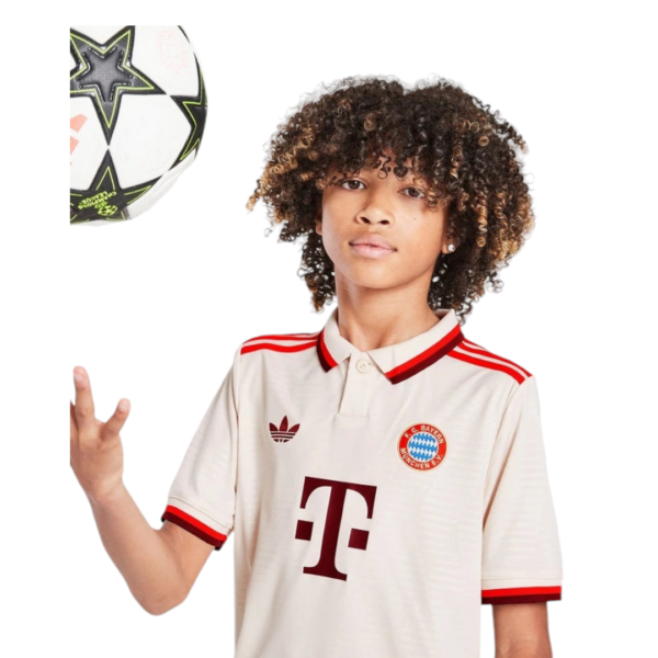 Young person wearing a cream Bayern Munich soccer jersey with red trim, reaching toward a ball hovering on the left side.