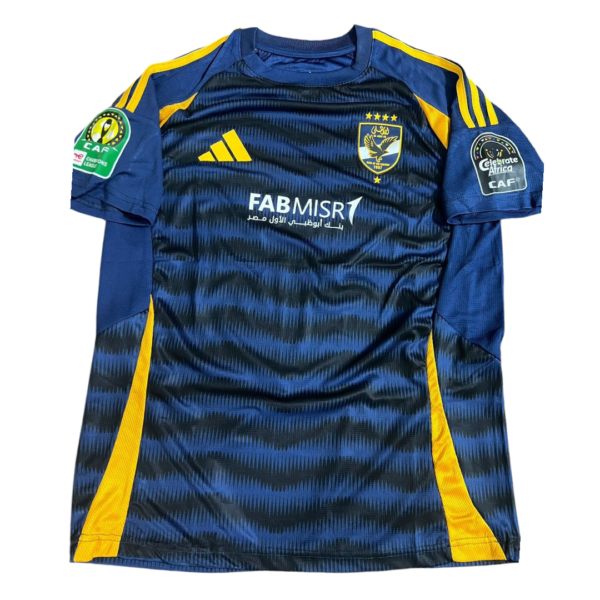 Blue and yellow soccer jersey laid flat, featuring a diagonal blue pattern, sponsor 'FAB MISR' on the chest and team crest. Patch logos on sleeves.