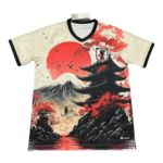 Beige V-neck T-shirt with a Japan-inspired print: a large red sun, Mount Fuji, a black pagoda, red maple trees, and a river scene with a Japan Football Association crest on the chest.