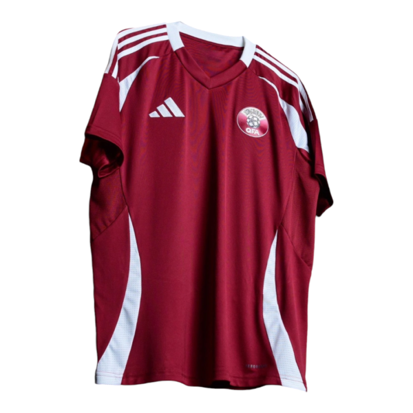 Front view of a maroon Adidas soccer jersey with white shoulder stripes, white side panels, and the QFA crest on the chest