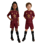 Two children in maroon Riyadh Season soccer kits stand side by side, smiling.