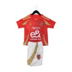 Red football jersey on a hanger with gold trim, crest, and sponsor text (Etisalat) visible on the chest area, paired with white shorts below.