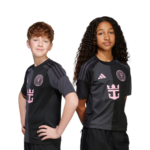 Two kids posing in black and gray soccer jerseys with pink logos, standing back-to-back with hands on hips on a white background.