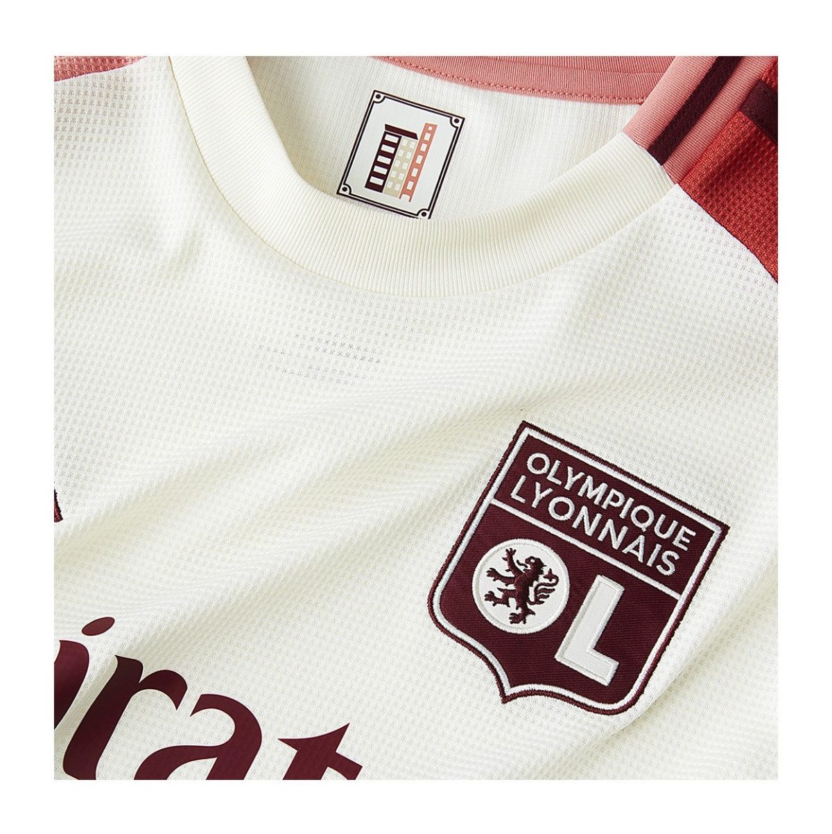 Close-up of a white Olympique Lyonnais soccer jersey, featuring the maroon crest with 'OLYMPIQUE LYONNAIS' and a white 'L' on the chest.