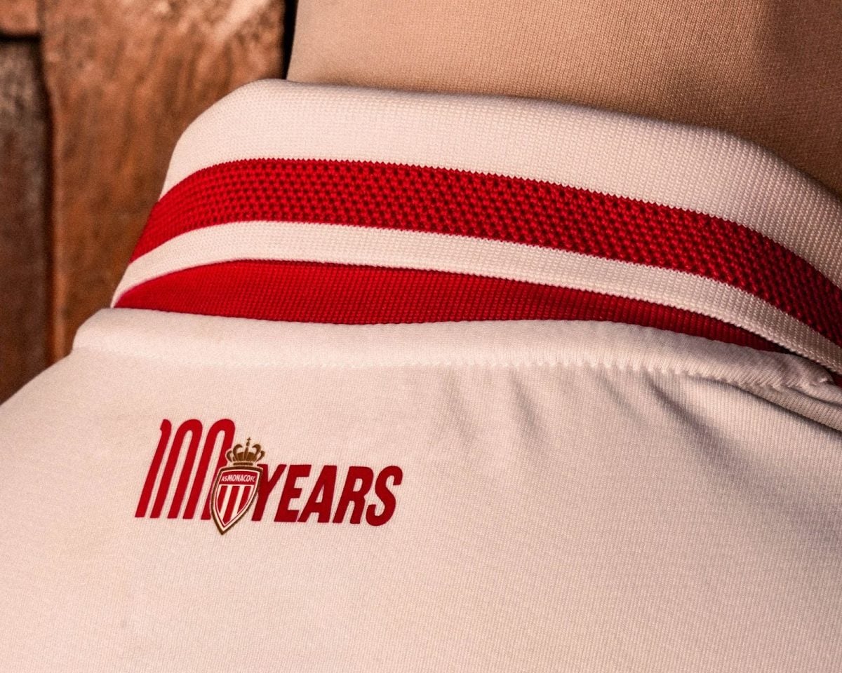 Close-up of white fabric with red stripe and a '100 YEARS' graphic and club crest