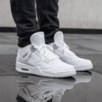 Pair of white sneakers with black jeans standing on wet pavement, their reflection visible in a puddle.
