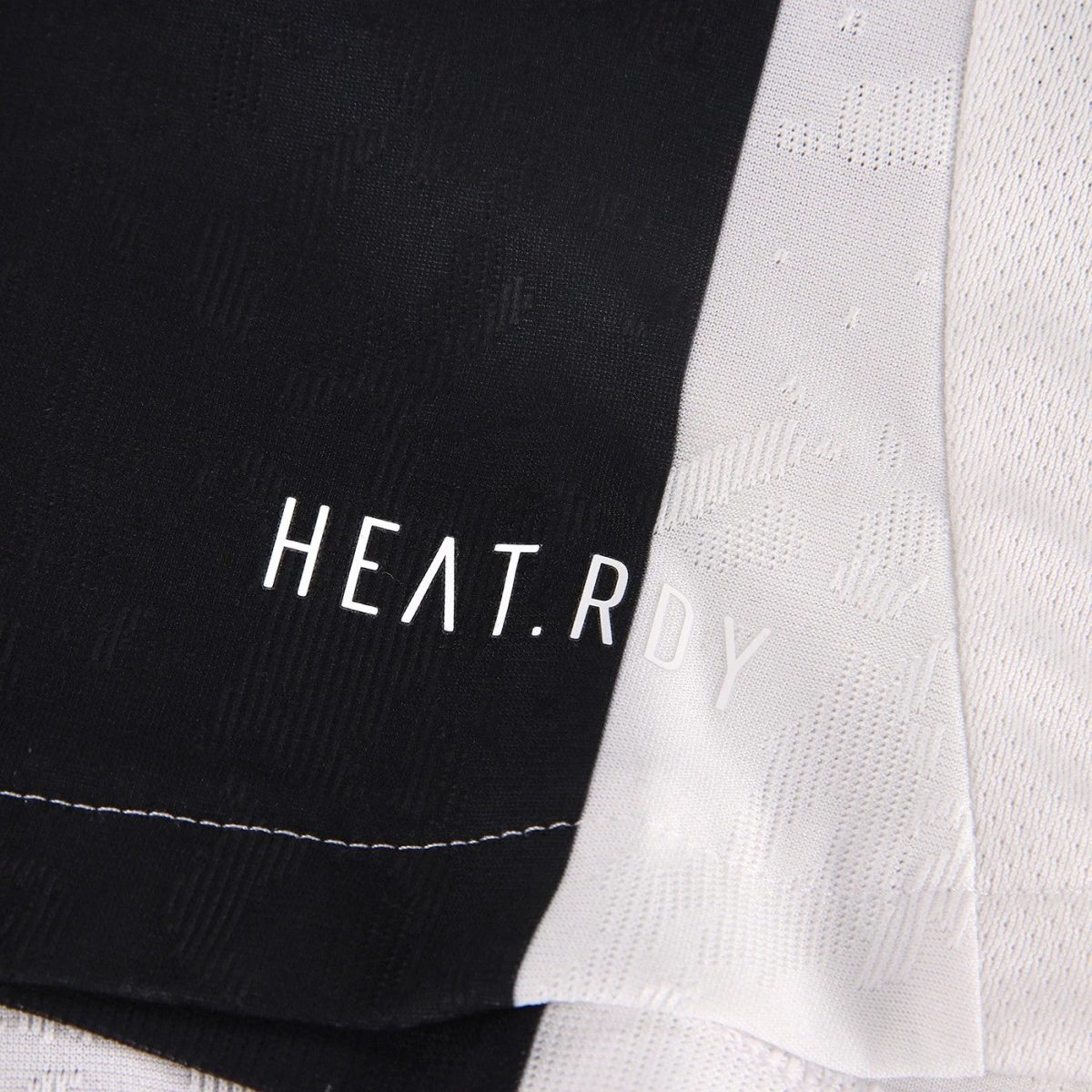 Close-up of a black fabric panel with white 'HEAT.RDY' branding, overlapped by a light gray patterned fabric.