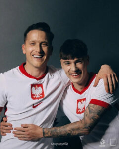 Two men in Poland national soccer jerseys smile with arms around each other in a friendly pose.