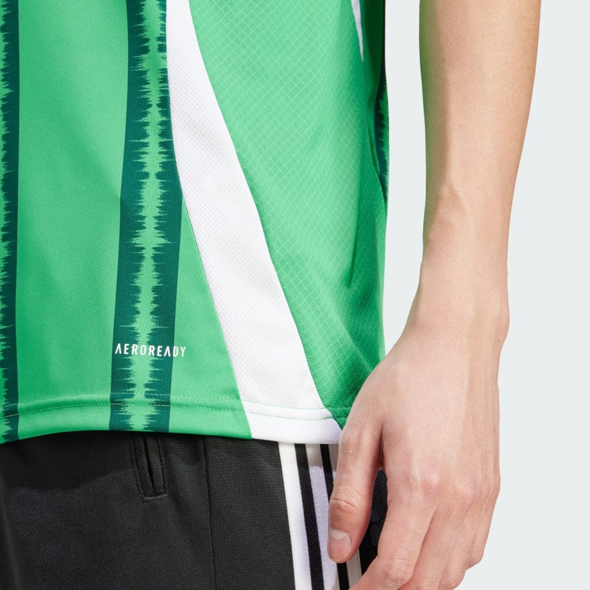 Close-up of a green athletic jersey with white diagonal stripe and 'AEROREADY' text, worn by a person whose arm is resting at their side.