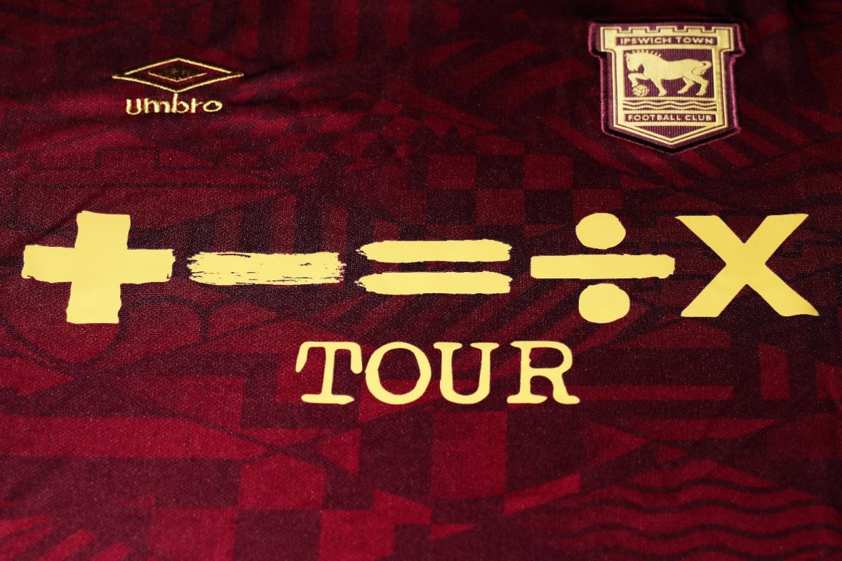 Close-up of a maroon Ipswich Town FC jersey with gold sponsor text and the club crest in the top right area, plus the Umbro logo near the left.