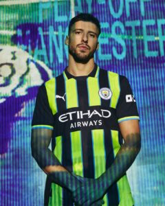 Man wearing a neon yellow-and-navy Manchester City jersey poses against a vibrant, abstract blue and purple background.