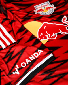 Close-up of a red and black sports jersey with the Red Bull logo and a New York emblem, featuring bold geometric patterns.