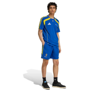 R | UAE SPORT STORE Male model in a blue Adidas soccer kit with yellow trim, standing with hands in pockets and looking forward.