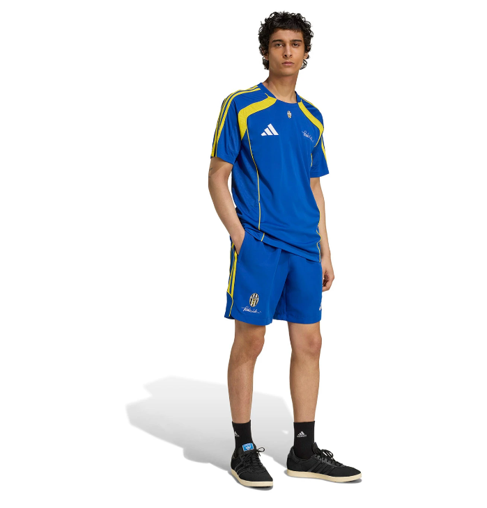 R | UAE SPORT STORE Male model in a blue Adidas soccer kit with yellow trim, standing with hands in pockets and looking forward.