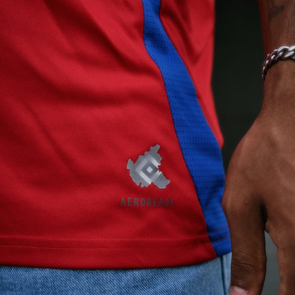 R5ys0GLV3VN51z0 | UAE SPORT STORE Close-up of a red athletic shirt with a blue stripe, showing the Aeroready logo near the hem.