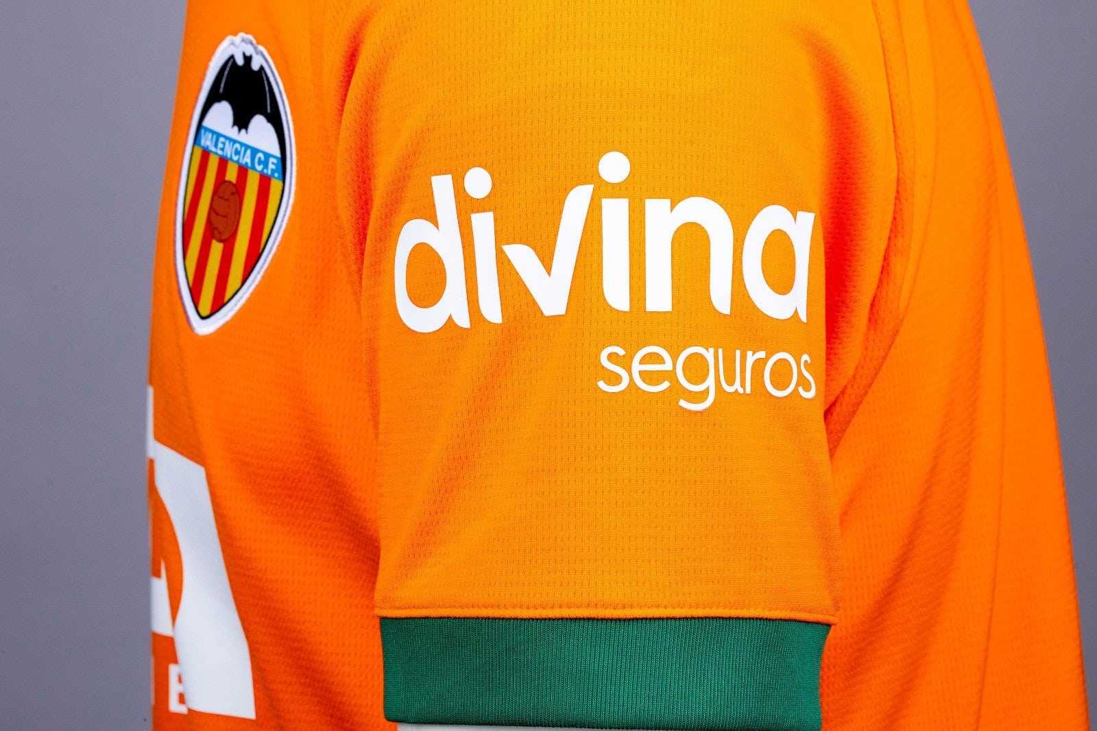 R6SkV5b0mv7wmwX | UAE SPORT STORE Close-up of bright orange Valencia CF jersey with sponsor 'divina seguros' and club crest on the sleeve.