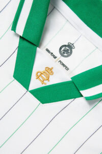 RACINGSHORTSLEEVE_04_600x_644608b4-72b7-40e3-895c-0010265c7f54 | UAE SPORT STORE Close-up of a white striped polo shirt with green collar trim and gold embroidery near the collar.