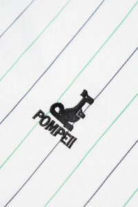 RACINGSHORTSLEEVE_05copia_600x_73756634-2a53-4316-964a-23e8be952999 | UAE SPORT STORE Embroidered sewing machine logo with the word POMPEI on white fabric with diagonal blue and green stripes.
