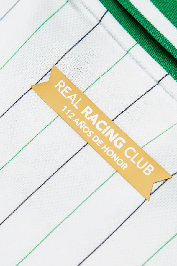 RACINGSHORTSLEEVE_07_600x_57887988-576a-40d7-9d85-fca909610b01 | UAE SPORT STORE Yellow ribbon badge on a white, striped sports fabric reads 'REAL RACING CLUB' with smaller text '112 AÑOS DE HONOR'.