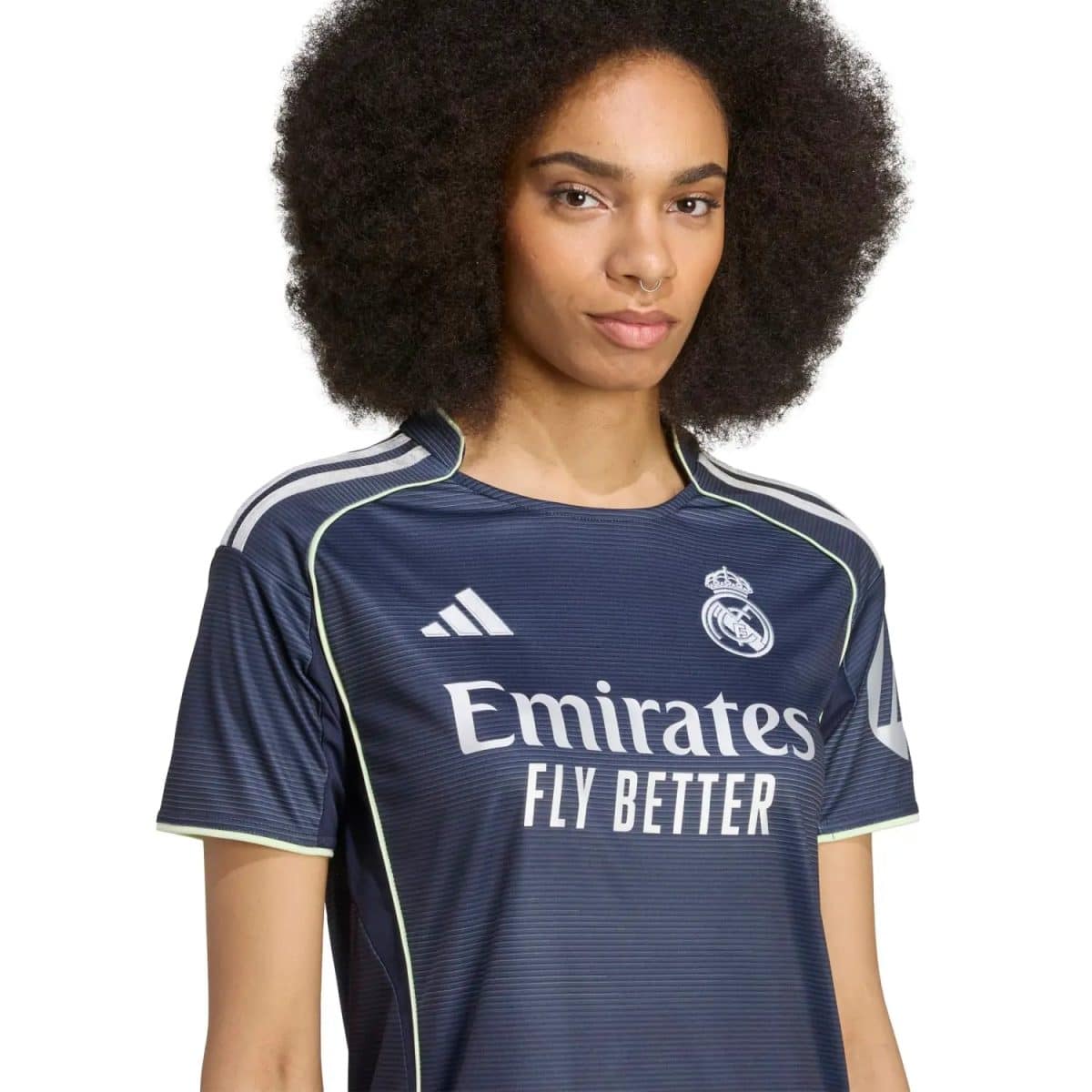 Portrait of a woman with an Afro hairstyle wearing a navy Real Madrid football jersey with the Emirates Fly Better slogan and club crest visible on the chest.