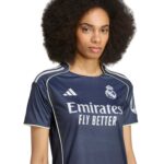 Portrait of a woman with an Afro hairstyle wearing a navy Real Madrid football jersey with the Emirates Fly Better slogan and club crest visible on the chest.