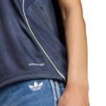 Close-up of a person wearing a dark athletic shirt with light green piping and jeans showing an Adidas trefoil logo.